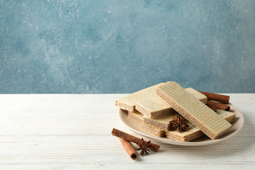 Plate with wafers and cinnamon on white wooden table, space for text