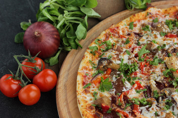 Italian concept, Italian cuisine. Pizza on a black background with fresh vegetables and herbs. Rustic.