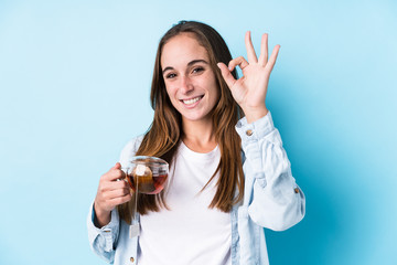 Young caucasian woman holding a tea isolated cheerful and confident showing ok gesture.