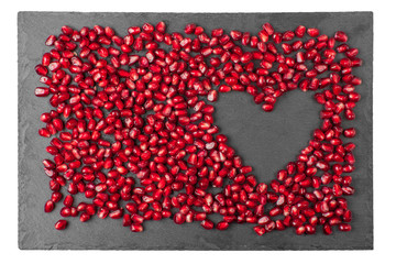 Festive romantic background for Valentine's day greeting post-card. Red pomegranate seeds on stone Board are laid out in shape of heart, symbol of love and loyalty. Blank for souvenir