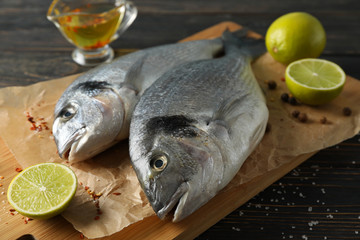 Cutting board with Dorado fishes, lime and spices on wooden background, close up