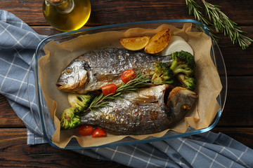 Baking tray with tasty dorado fish on wooden background, top view 