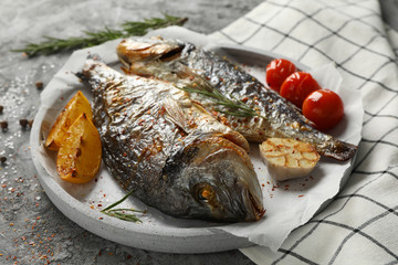 Plate with baked Dorado on garnished grey background, close up