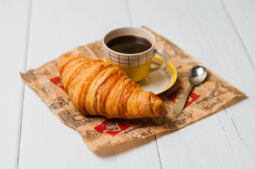 Espresso coffee in vintage yellow cup with a saucer and spoon, croissants on craft paper, on a light background, breakfast concept
