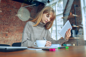 Obraz premium Beautiful caucasian business lady working in office with laptop. Young female model in co-working place makes notes, drinks coffee, performes tasks. Concept of business, finance, freelance, open space