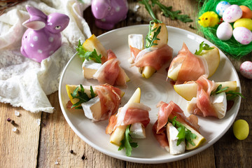 Festive snacks. Pear appetizer with jamon, arugula and brie cheese on a rustic wooden table.