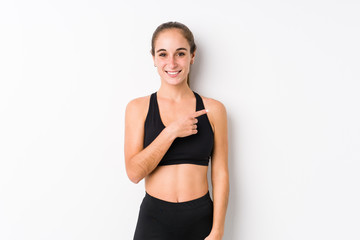 Young caucasian fitness woman posing in a white background smiling and pointing aside, showing something at blank space.