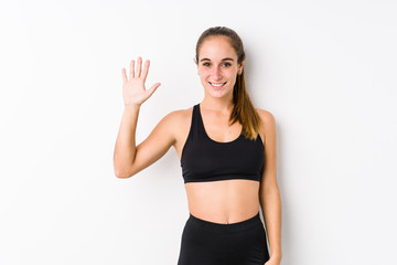Fototapeta na wymiar Young caucasian fitness woman posing in a white background smiling cheerful showing number five with fingers.
