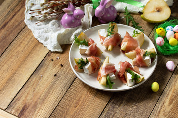 Festive snacks. Pear appetizer with jamon, arugula and brie cheese on a rustic wooden table. Copy space.