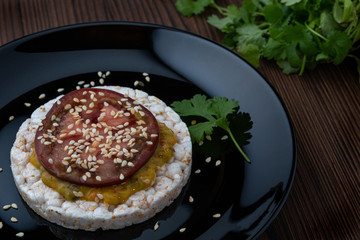 Rice galettes with sauce and tomato on black plate. Light breakfast.