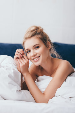 cheerful young woman lying in sheets on bed in morning