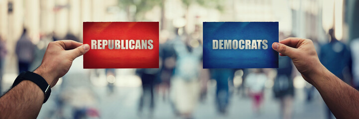 Two hands holding different colored paper sheet as Republicans versus Democrats political party over crowded street background. Future strategy concept red vs blue, Donkeys or Elephants symbols.