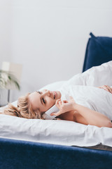 Obraz na płótnie Canvas beautiful happy woman talking on smartphone in bed in morning