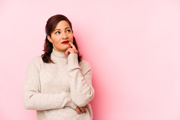 Fototapeta premium Middle age latin woman isolated on a pink background looking sideways with doubtful and skeptical expression.