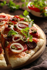 Italian cuisine. Pizza with salami and sausage on a wooden background with tomatoes, herbs and onions. Rustic