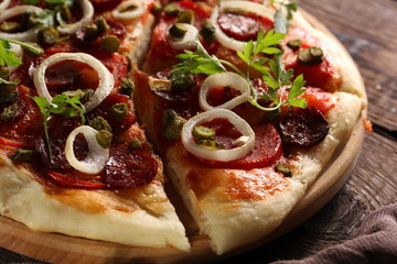 Italian cuisine. Pizza with salami and sausage on a wooden background with tomatoes, herbs and onions. Rustic