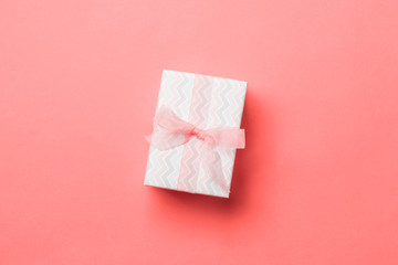 wrapped Christmas or other holiday handmade present in paper with pink ribbon on living coral background. Present box, decoration of gift on colored table, top view with copy space