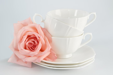 Obraz na płótnie Canvas White porcelain cup with a saucer for tea or coffee and pink rose, demitasse or teacup. Crockery on white background.