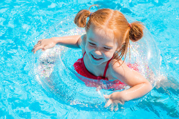 Fototapeta na wymiar little redhead girl swims on a transparent swimming circle