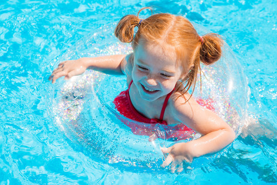 little redhead girl swims on a transparent swimming circle