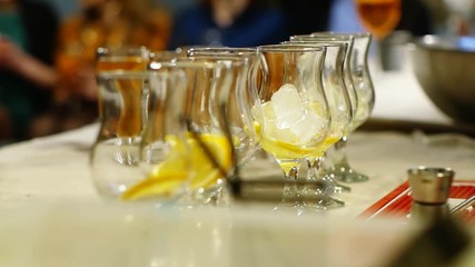 Professional barman puts ice and oranges in glasses with cocktails