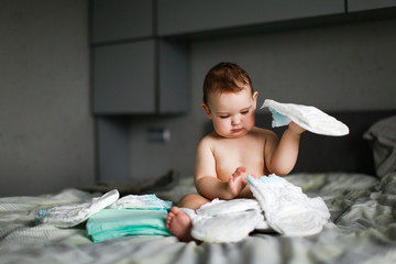 Cute chubby baby sitting with disposable diapers - obrazy, fototapety, plakaty