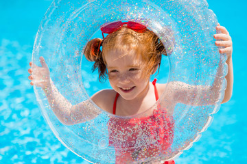 little red-haired girl in a red swimsuit and heart - shaped sunglasses holds a swimming circle in...