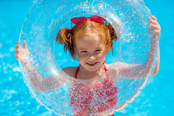 little red-haired girl in a red swimsuit and heart - shaped sunglasses holds a swimming circle in...