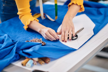Creative caucasian fashion designer standing in her studio and drawing scheme on blue linen for a beautiful evening dress.