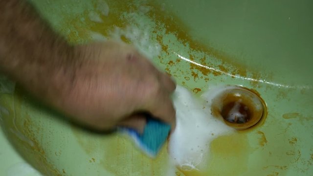 Human hand washes and cleans a dirty sink in rust with foam and sponge. Homework concept. Close-up.