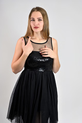 Fototapeta premium A photo of a pretty smiling girl with long hair and excellent make-up in a black dress is standing in various poses in the studio. Universal concept vertical woman portrait on a white background.