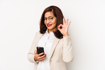 Fototapeta premium Middle age latin woman holding a mobile phone isolated cheerful and confident showing ok gesture.