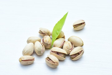  Pistachios on the white wooden background, accompanied by green leaf