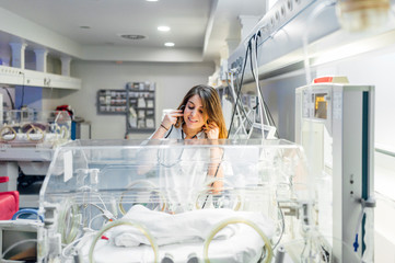 Nurse gently touching fragile newborn in neonatal incubator - obrazy, fototapety, plakaty