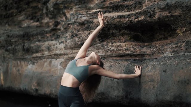 Woman doing stretching exercises and dances on beach near cliff, slow motion