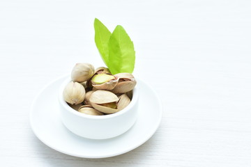  Pistachios on the white wooden background, accompanied by green leaf