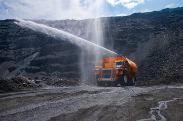 Heavy truck pours the road with water in the iron ore quarry. Dust removal, protection of the environment. Irrigation of the road from dust