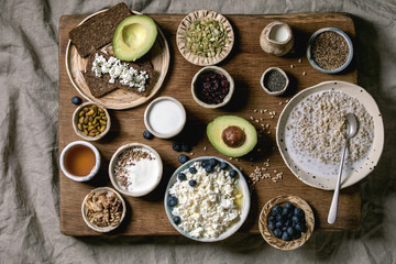 Healthy breakfast. Variety of breakfast dishes wheat, yogurt, kefir, cottage cheese, avocado, rye bread, seeds, nuts and berries assortment in ceramic bowls. Wooden and textile background. Flat lay