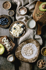 Obraz na płótnie Canvas Healthy breakfast. Variety of breakfast dishes sprouted wheat, yogurt, kefir, cottage cheese, avocado, rye bread, seeds, nuts and berries assortment in ceramic bowls over wooden background. Flat lay
