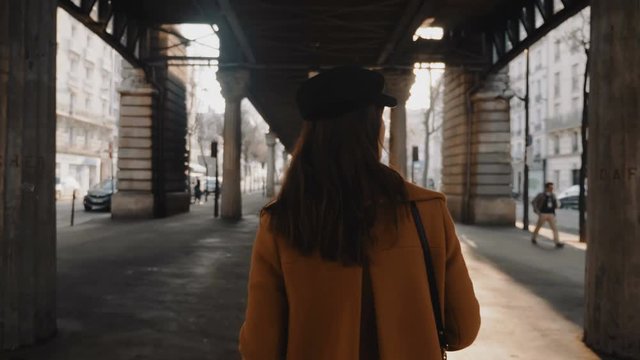Rear view happy stylish fashion blogger woman exploring Paris streets under sunny high line metro flyover slow motion.