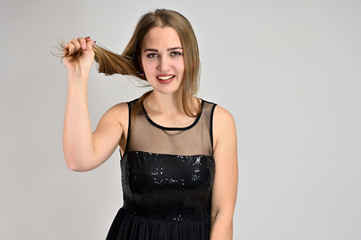 Fototapeta premium Universal concept horizontal portrait of a woman on a white background. A photo of a pretty smiling girl with long hair and excellent make-up in a black dress stands in different poses.