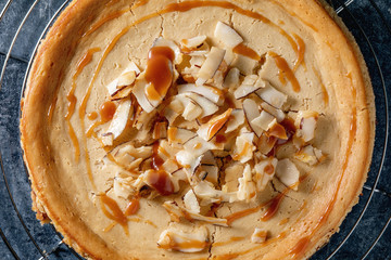 Homemade cane sugar baked cheesecake on cooling rack with caramelized coconut and caramel topping over blue texture background. Close up. Flat lay, space