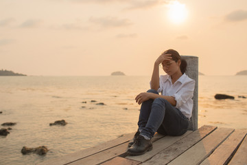 Woman sitting alone With anxiety And disappointed in the stories In the setting sun At the wooden bridge in the ocean