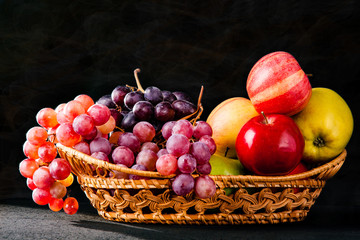 Grapes and apples in a wicker basket on a dark background