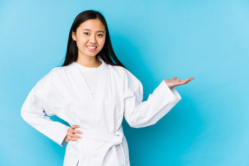 Young chinese woman practicing karate isolated showing a copy space on a palm and holding another hand on waist. © Asier