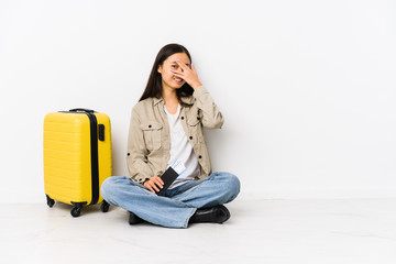 Young chinese traveler woman sitting holding a boarding passes blink at the camera through fingers, embarrassed covering face.