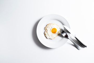 Friied egg on plate and white background. Highly contrasted image.
