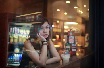 Young Girl waiting someone who late , Chin in hand , and looking out behind the cafe window , moment of enjoy her tea time deep thinking in hong kong