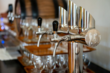 Chrome-plated tap for filling drinks with a blurry image of glasses in the background. Side view. Selective focus.