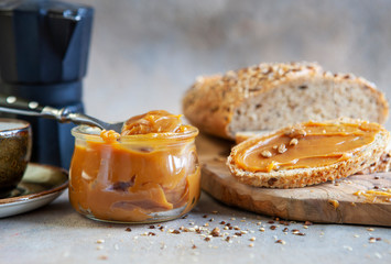 Glass jar of homemade salted caramel sauce with bread and walnuts. Close up